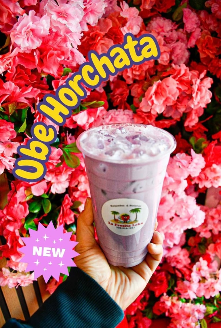 Hand holding a Ube Horchata beverage against blooming pink and red flowers with NEW sticker and product label visible
