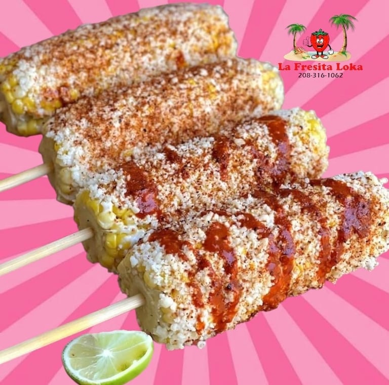 Three elote corn cobs coated in mayo, cheese, and chili powder on sticks with lime wedge on pink background