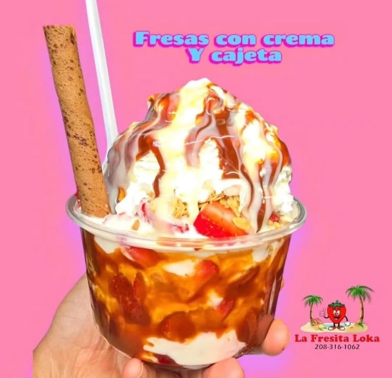 Hand holding iced coffee drink with whipped cream, caramel drizzle, cookie, and fresh strawberry on pink background. Spanish text reads Fresas con crema y cajeta