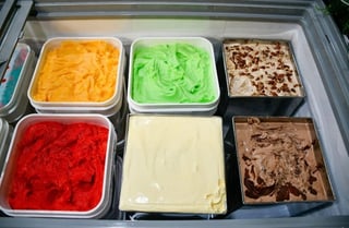 Six containers of colorful gelato flavors in a display case