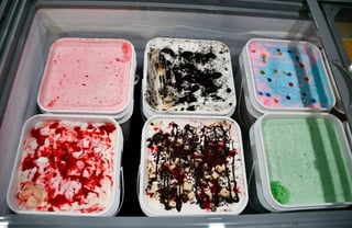 Six flavors of ice cream in white square containers displayed in a freezer case