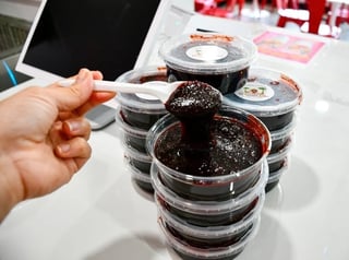 Hand holding makeup brush with chocolate-colored sparkly cosmetic product stacked in clear containers