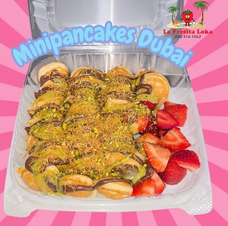 Clear container of mini pancakes topped with pistachio powder and garnished with fresh strawberries